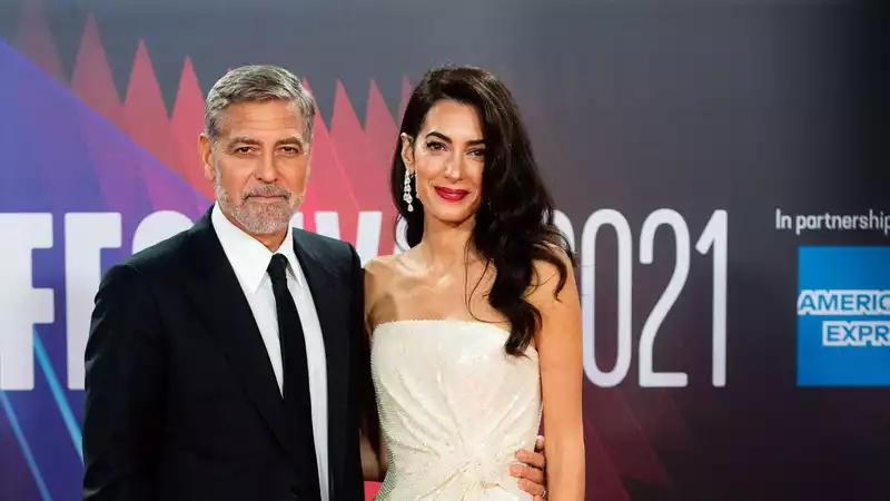 George Clooney helps Amal out of her costume on the red carpet.