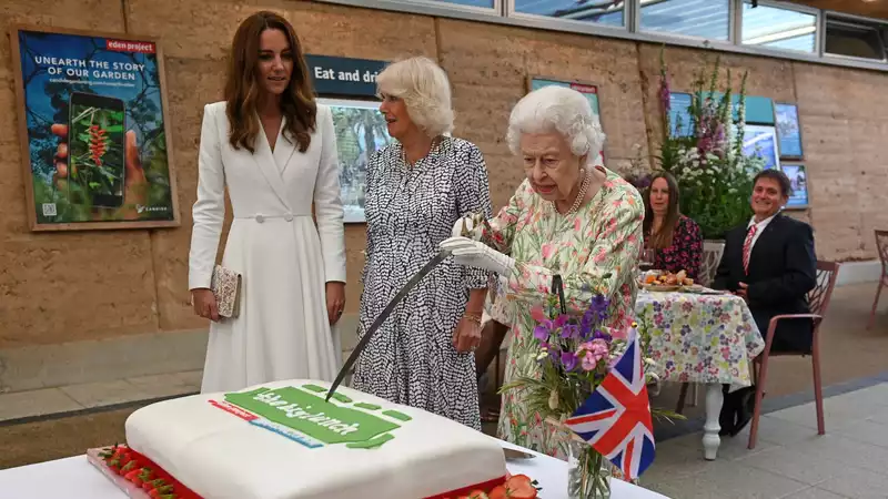 Queen Elizabeth cuts the cake with a ceremonial sword.