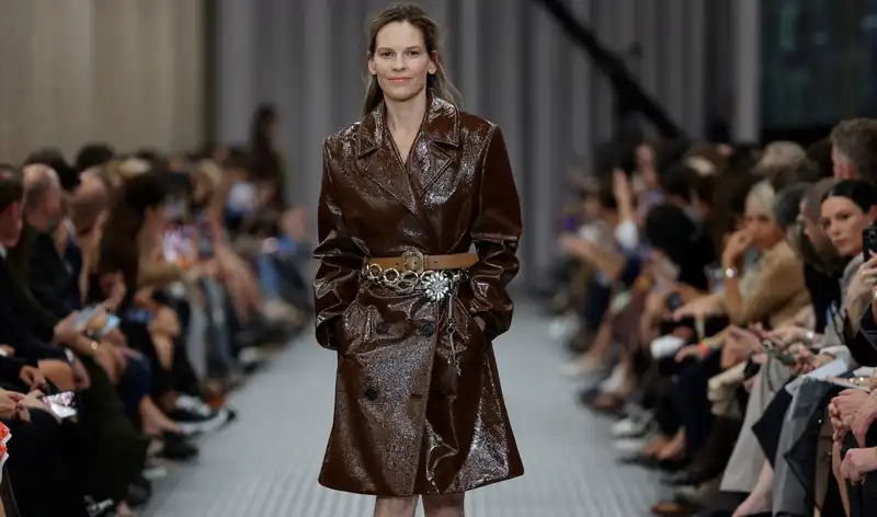 Hilary Swank surprise walks the Miu Miu runway at Paris Fashion Week in a triple-belted trench coat and almost no makeup.