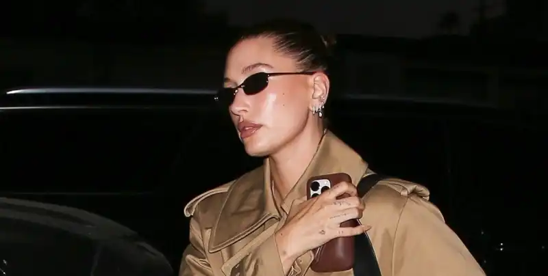 Hailey Bieber remixes her rich-girl fall uniform with a shiny khaki trench coat and blue loafers